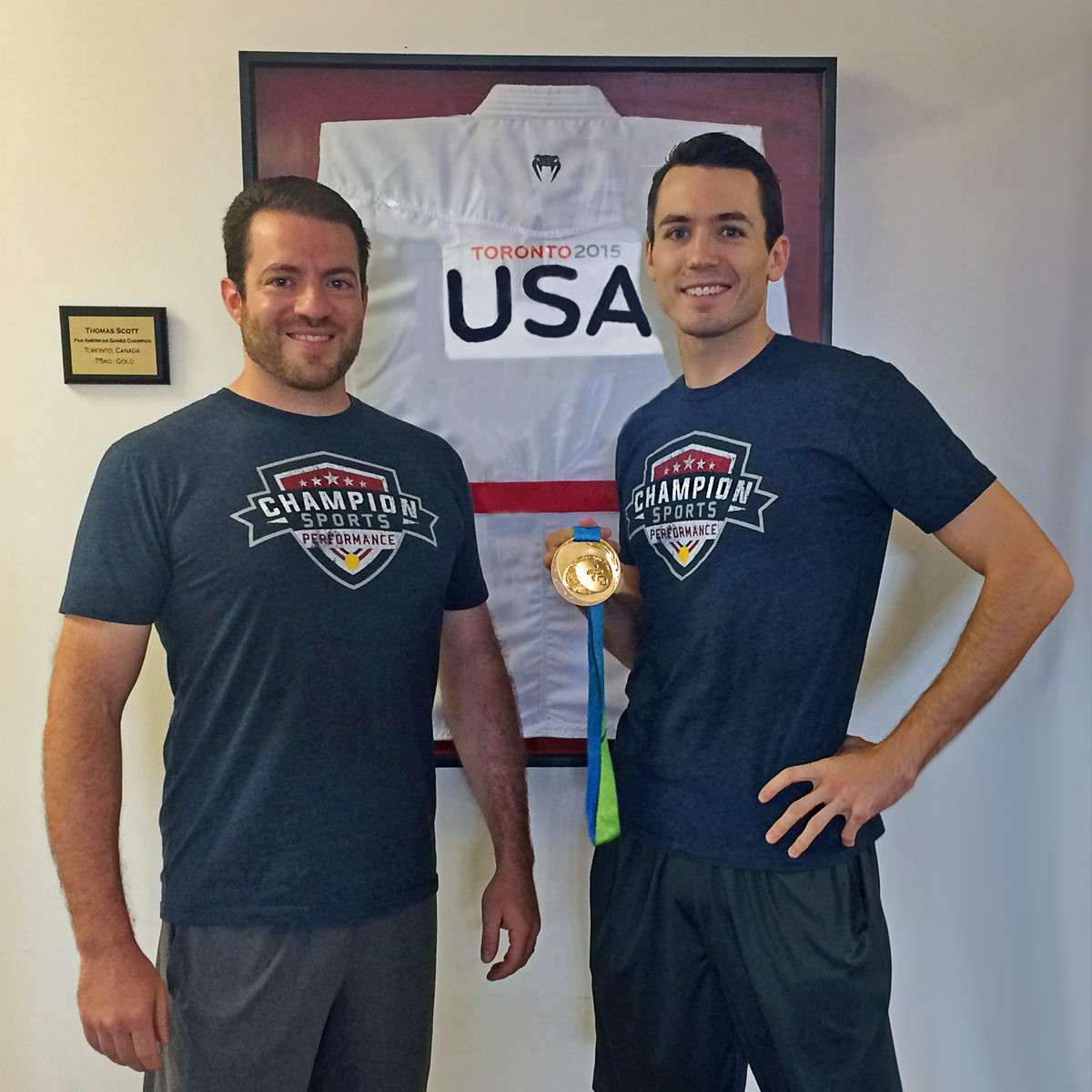 Champion Sports Performance Coach Chris Stratis and Athlete Tom Scott with his Pan American Games gold medal and his framed gi from the competition.